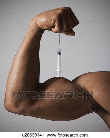 Stock Image - Syringe perched on a flexed muscular arm. Fotosearch