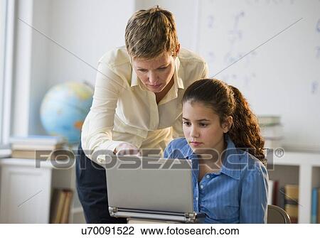 Stock Image - Teacher helping student in classroom. Fotosearch