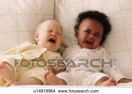Picture - Two babies crying on a couch. Fotosearch