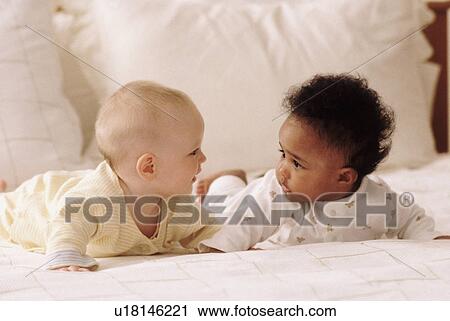 Stock Image - Two babies lying on a bed together. Fotosearch