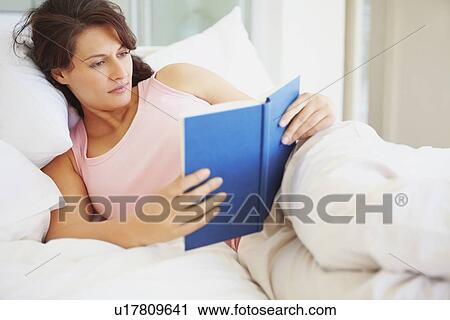 Stock Image - Woman reading in bed. Fotosearch