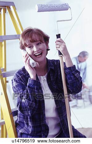 Stock Photo - Woman talking on phone while holding a paint roller. Fotosearch