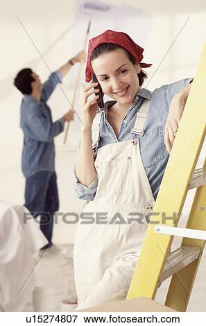 Stock Photo - Woman talking on phone while taking a break from painting. Fotosearch