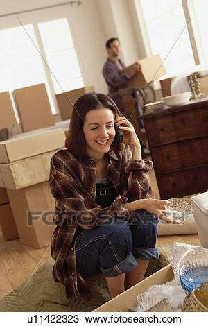 Stock Image - Woman talking on the phone while unpacking boxes. Fotosearch