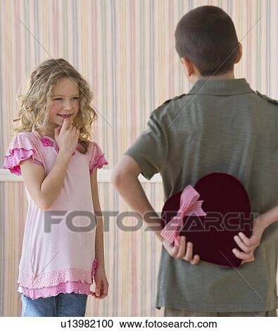 Stock Image - Young boy hiding a box of chocolates from young girl. Fotosearch