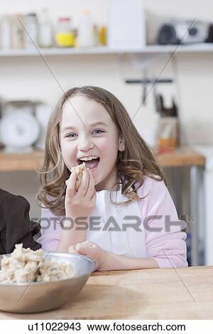 Stock Image - Young girl eating cookie batter. Fotosearch