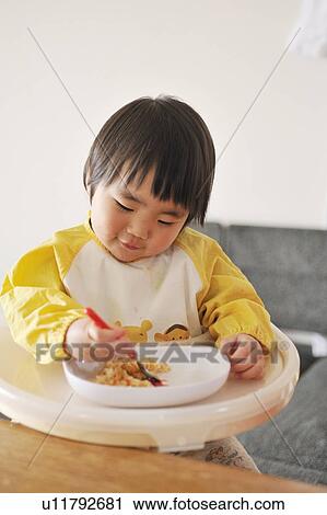 Stock Image - Baby boy sitting in high chair, eating baby food. Fotosearch