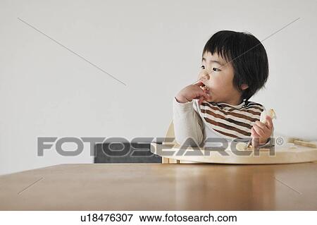 Baby boy sitting in high chair, eating bread View Large Photo Image Stock Photo - Baby boy sitting in high chair, eating bread. Fotosearch
