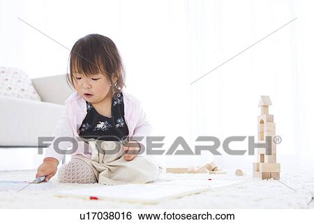 Stock Photograph - Baby girl choosing crayons next to wooden building blocks. Fotosearch