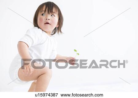 Stock Photo - Baby girl crouching and holding sapling. Fotosearch