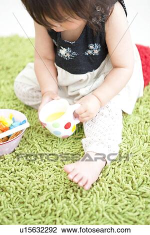 Stock Image - Baby girl holding a cup of orange juice. Fotosearch