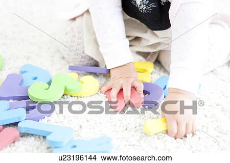 Picture - Baby girl holding alphabet and number toys. Fotosearch