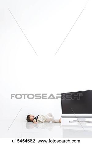 Stock Image - Baby girl lying on back near TV. Fotosearch