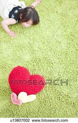 Stock Image - Baby girl lying on front and heart shaped cushions. Fotosearch
