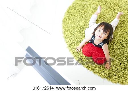 Picture - Baby girl lying on front watching TV. Fotosearch