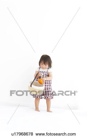 Stock Photo - Baby girl putting orange inside a basket. Fotosearch
