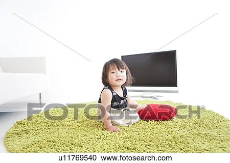Stock Image - Baby girl sitting on a rug. Fotosearch