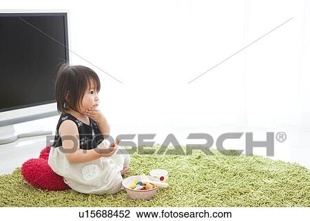 Stock Image - Baby girl sitting on cushion holding dessert. Fotosearch