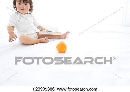 Stock Photograph - Baby girl with book and orange. Fotosearch