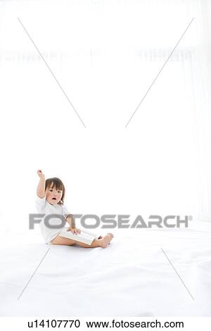 Stock Image - Baby girl with open book and hand raised. Fotosearch