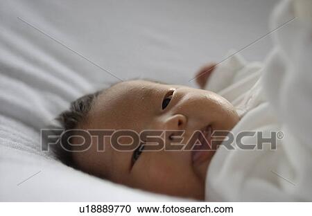 Stock Image - Baby lying on bed, close up. Fotosearch