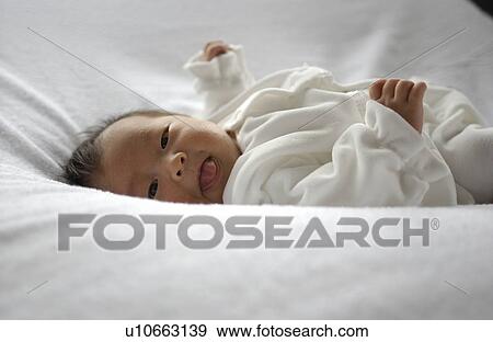 Stock Photo - Baby lying on bed, looking at camera. Fotosearch
