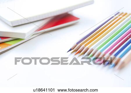 Stock Image - Colored pencils and note pads on white background, close up. Fotosearch