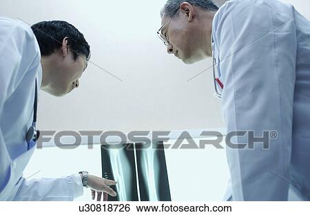 Stock Photograph - Doctors discussing X-rays, white background. Fotosearch