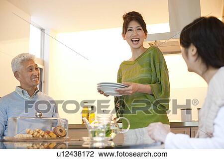 Stock Image - Family in dining room, daughter holding plates, smiling. Fotosearch