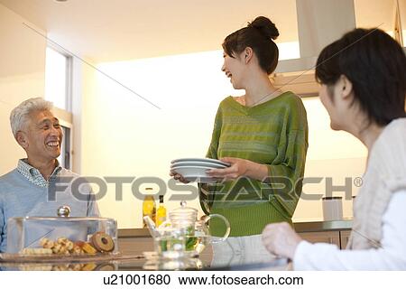 Stock Image - Family in dining room, daughter holding plates, smiling. Fotosearch