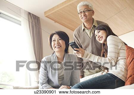 Stock Image - Family in living room, daughter holding remote control. Fotosearch