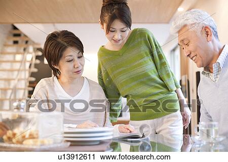 Stock Image - Family reading magazine in dining room, smiling. Fotosearch