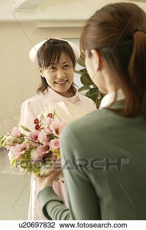Stock Image - Female nurse giving flower bouquet to woman. Fotosearch