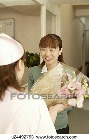 Stock Image - Female nurse giving flower bouquet to woman. Fotosearch