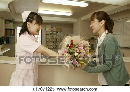Stock Photography - Female nurse giving flower bouquet to woman, smiling. Fotosearch