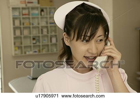 Stock Image - Female nurse using phone at nurses station, smiling. Fotosearch