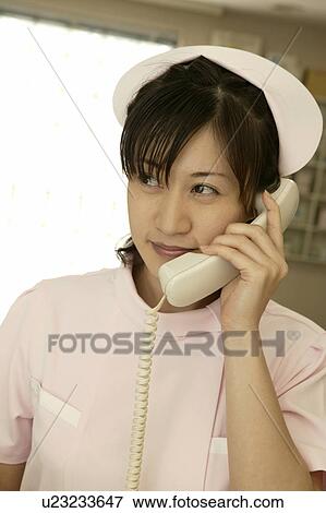 Stock Photo - Female nurse using phone at nurses station, smiling. Fotosearch