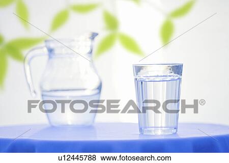 Stock Photo - Glass and pitcher with water on table, white background. Fotosearch