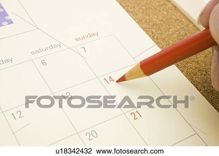 Stock Image - Hand writing on calendar with red pencil, close up. Fotosearch