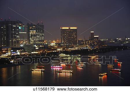 Stock Photo - Illuminated office buildings and boats in the night, long exposure, Tokyo prefecture, Japan. Fotosearch