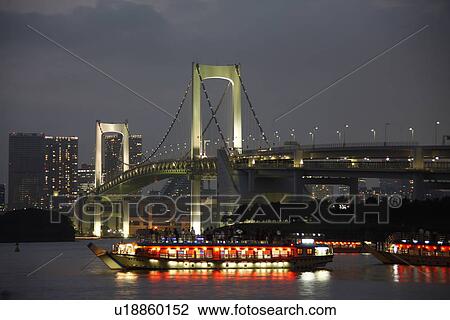 Stock Image - Illuminated Rainbow Bridge and boats in the night, long exposure, Tokyo prefecture, Japan. Fotosearch