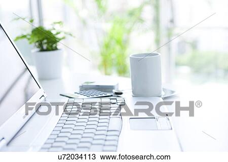 Stock Image - Laptop and cup of coffee on desk in office, differential focus. Fotosearch