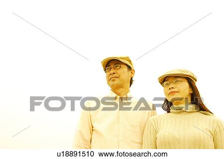 Stock Image - Mature couple in flat cap looking away, white background. Fotosearch