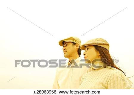 Stock Photograph - Mature couple in flat cap looking away, white background, copy space. Fotosearch
