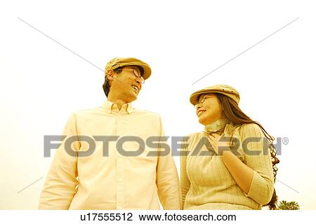Stock Image - Mature couple in flat cap smiling and looking at each other, white background. Fotosearch