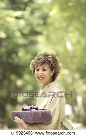 Stock Photo - Mature woman in Kimono holding gift, smiling, Kyoto city, Kyoto prefecture, Japan. Fotosearch