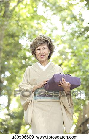 Stock Photo - Mature woman in Kimono holding gift, smiling, Kyoto city, Kyoto prefecture, Japan. Fotosearch