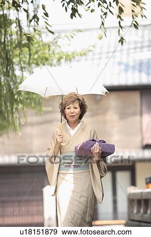 Stock Photo - Mature woman in Kimono holding umbrella and gift, Kyoto city, Kyoto prefecture, Japan. Fotosearch