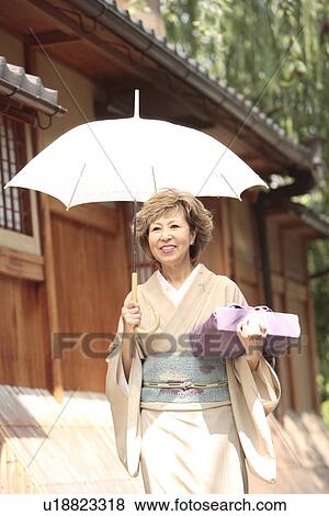 Stock Photo - Mature woman in Kimono holding umbrella and gift, Kyoto city, Kyoto prefecture, Japan. Fotosearch