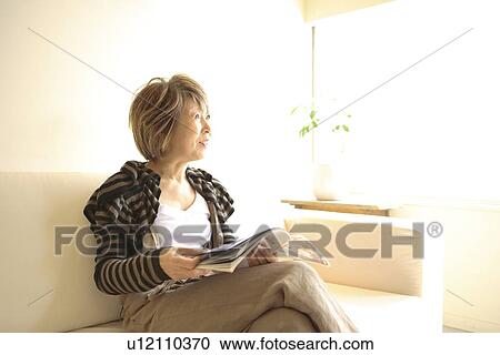 Mature woman sitting on sofa, holding magazine View Large Photo Image Stock Image - Mature woman sitting on sofa, holding magazine. Fotosearch
